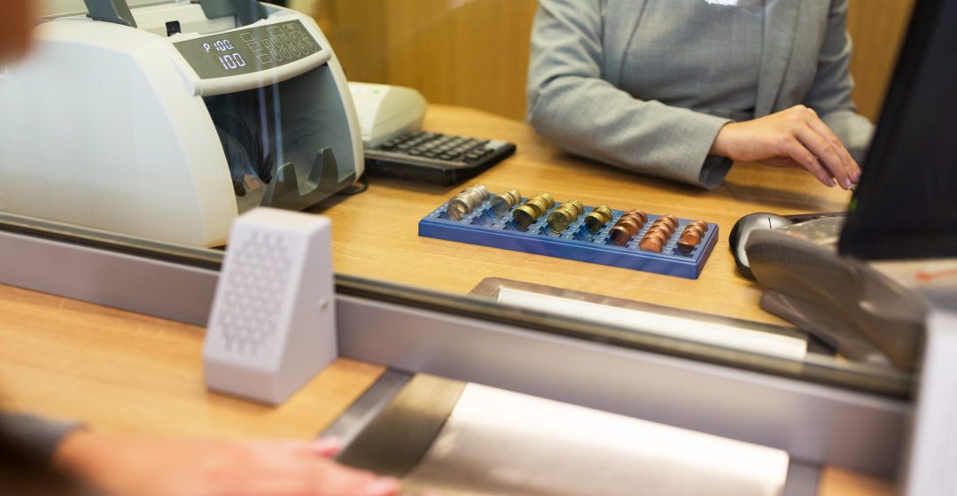 people, money, saving and finance concept - clerk counting coins for customer at bank office or currency exchanger