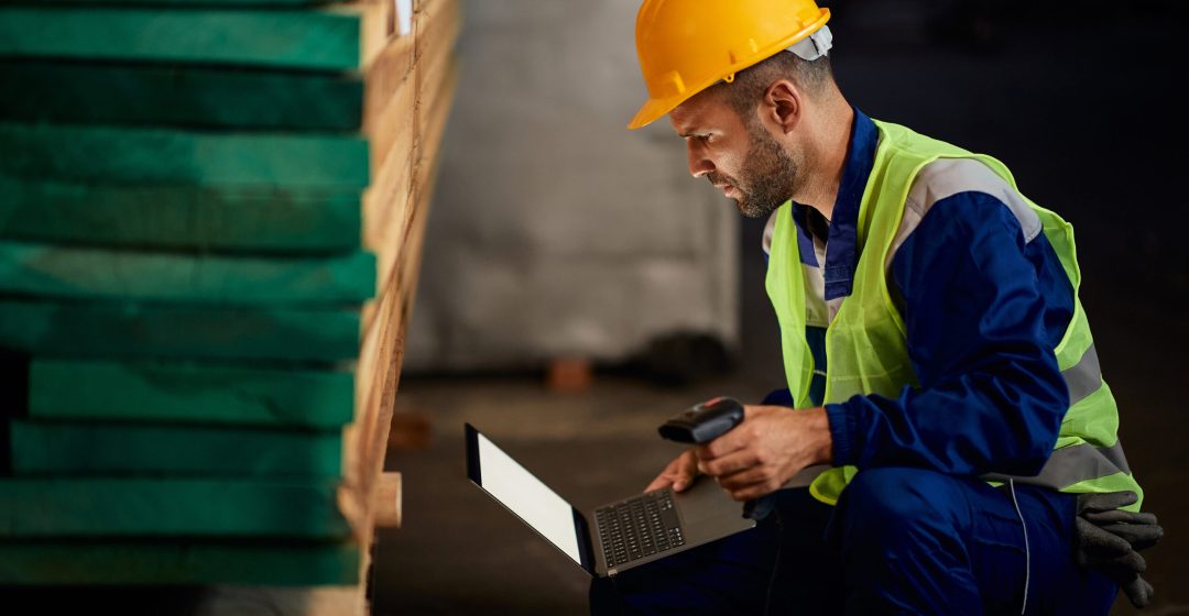 Male worker using bar code scanner and laptop while working at distribution warehouse.